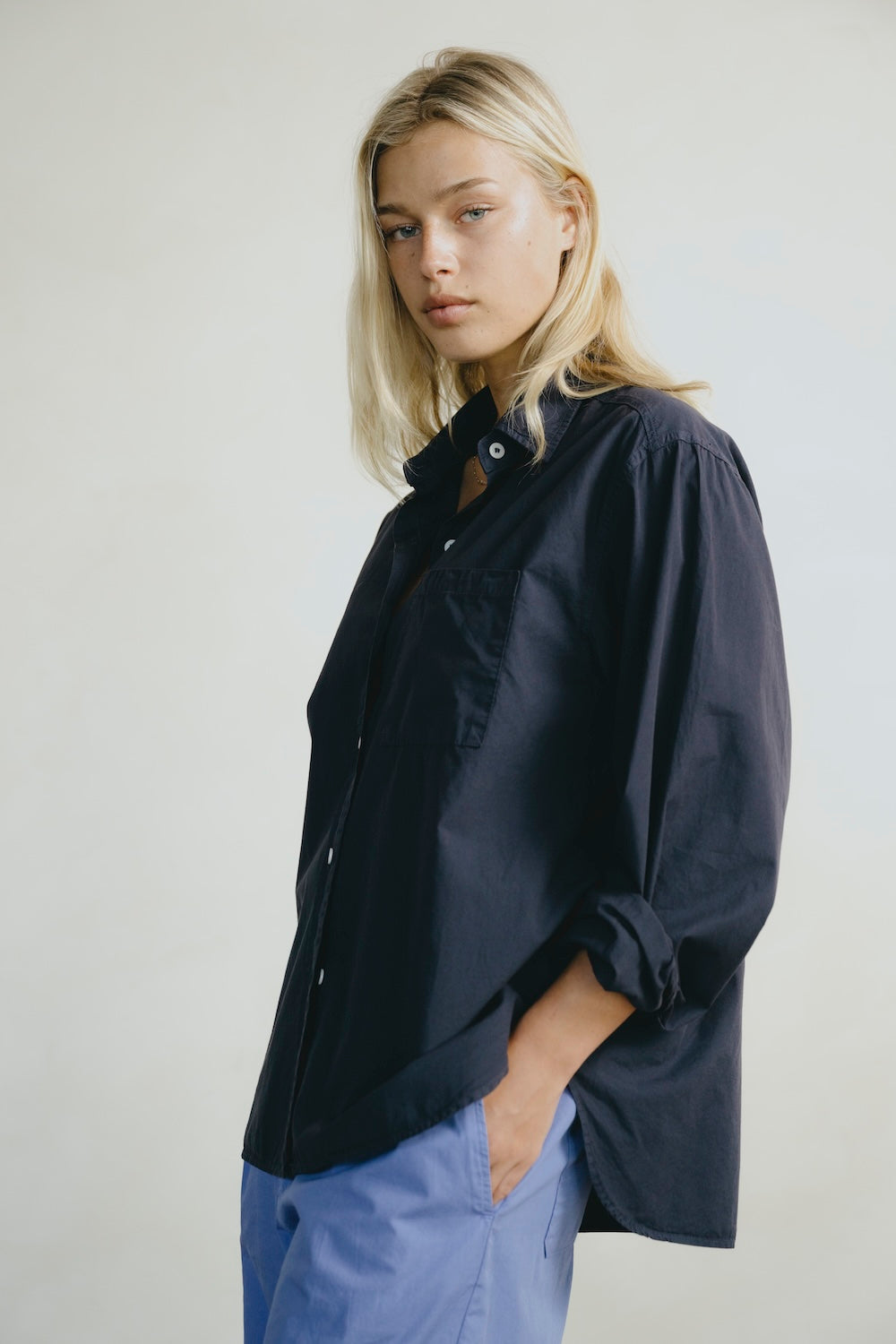 Woman wearing a dark blue shirt and light blue pants against a plain background