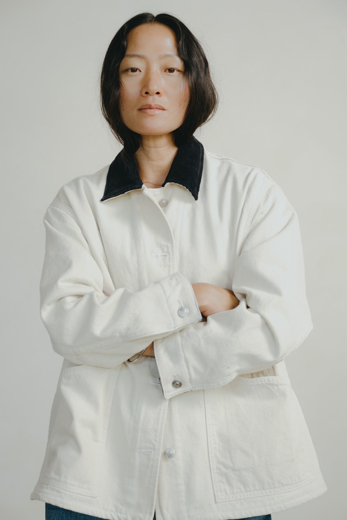 A model wearing an oversized off-white utility jacket with a contrasting black collar, standing against a neutral light gray background.