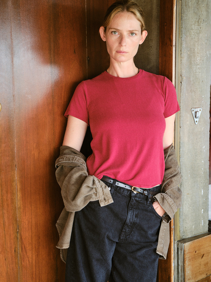 A woman standing against a wood doorway in a red crewneck tshirt.